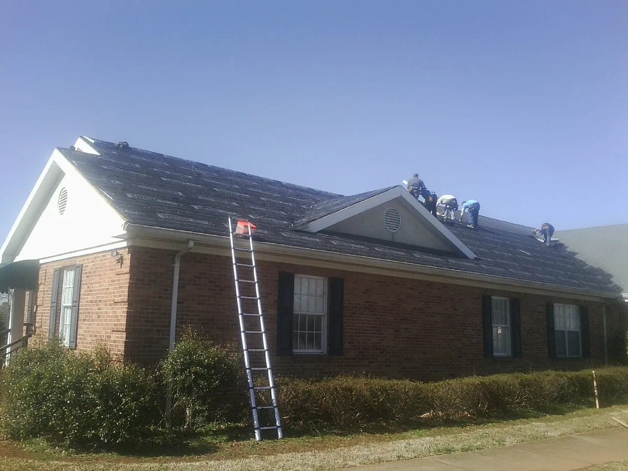 Crew tearing shingles off a brick ranch roof with a ladder set — Metal Roof Repair work by our crew in Osakis