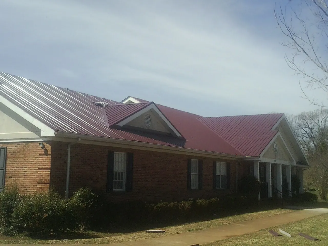 Red metal roof with gabled entries on a long brick building, from a Hail Damage Roof Repair job in Osakis