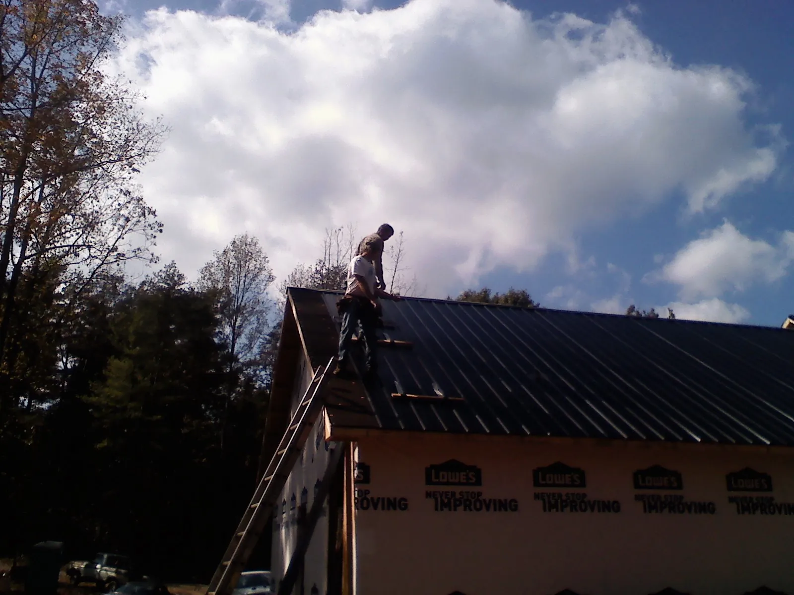 Roofer fastening dark metal panels high against a cloudy sky, from a Roof Inspection job in Osakis